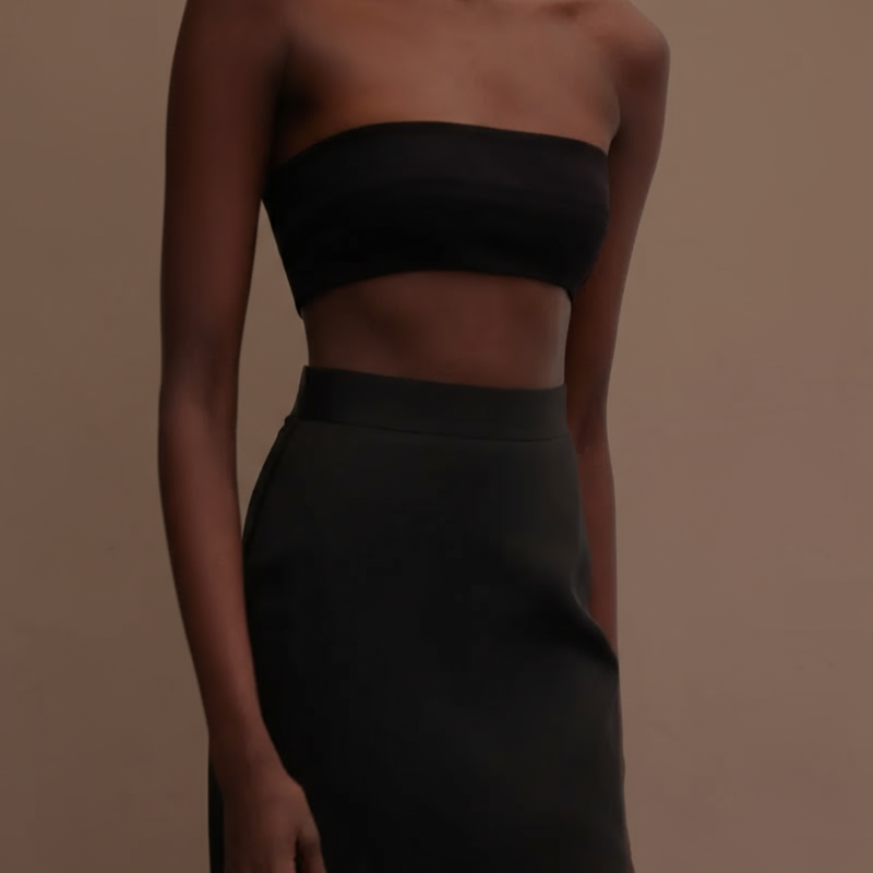 Woman wearing a black strapless top and skirt against a neutral background